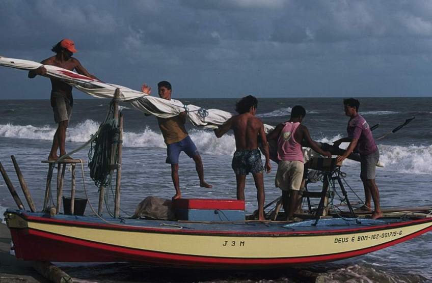 Jangadeiros standing on one of the larger jangadas preparing the mast to be raised.