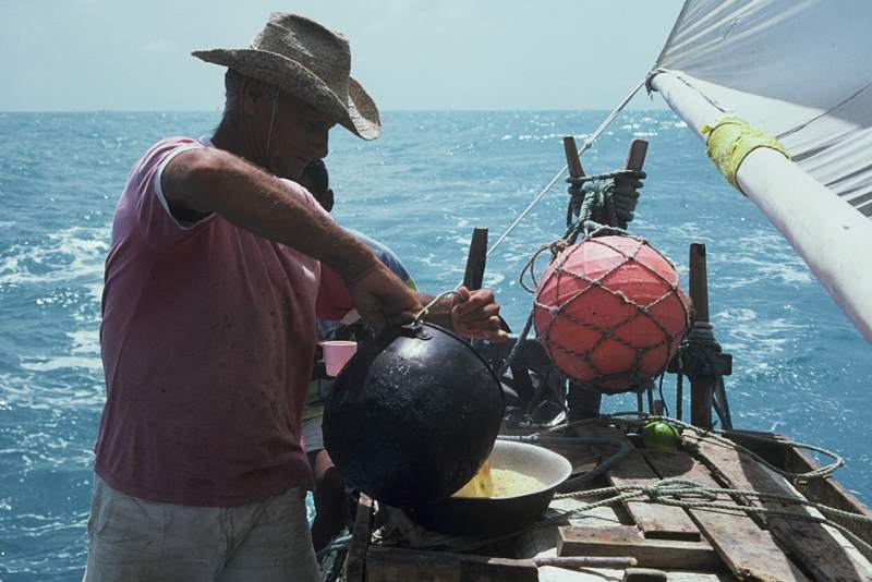 A jangadeiro is pouring broth from the cooking pot into a pan filed with farinha