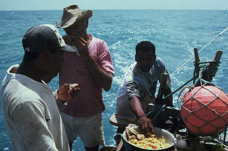 There jangadeiros eating fish and pirão while sailing.