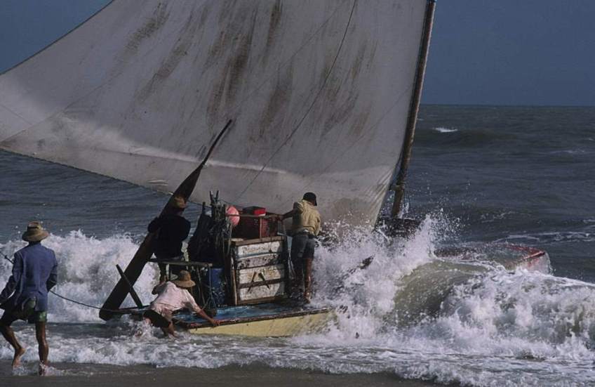 A jangada being pushed off as it leaves the beach.