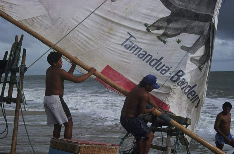 Two jangadeiros running the boom out to set the sail.