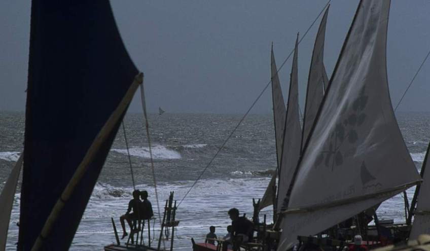 Looking through several sails drying on the beach to one lone jangada sail towards the horizon.