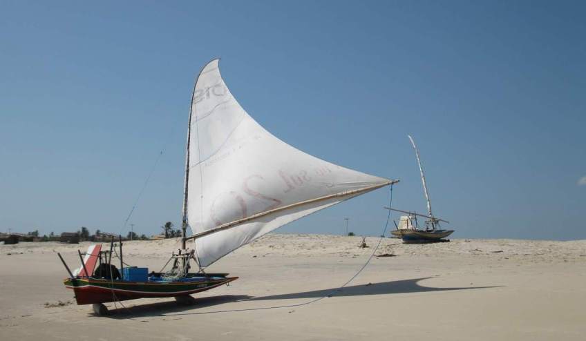 A paquete on the beach with its sail up to dry out in the wind.