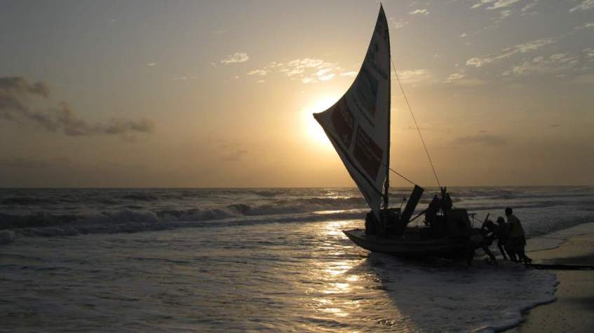 Fishermen pushing a jangada into the sea at sunrise.