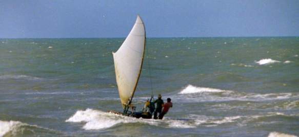 Two men on a jangada, sailing through whitecaps.